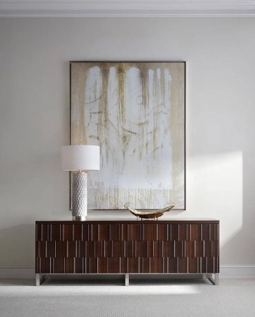 minimalist interior space with a large abstract artwork hanging above a modern wooden credenza or cabinet, accompanied by a table lamp